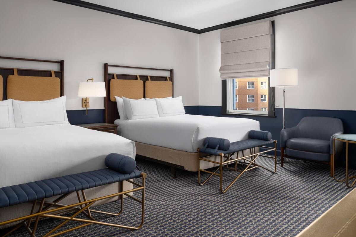 A hotel room with two beds, a seating area, and a window with a view.