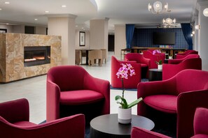 A modern lounge area with red upholstered chairs, a fireplace, a television, and a bookshelf. - Hilton Orrington / Evanston (Evanston)