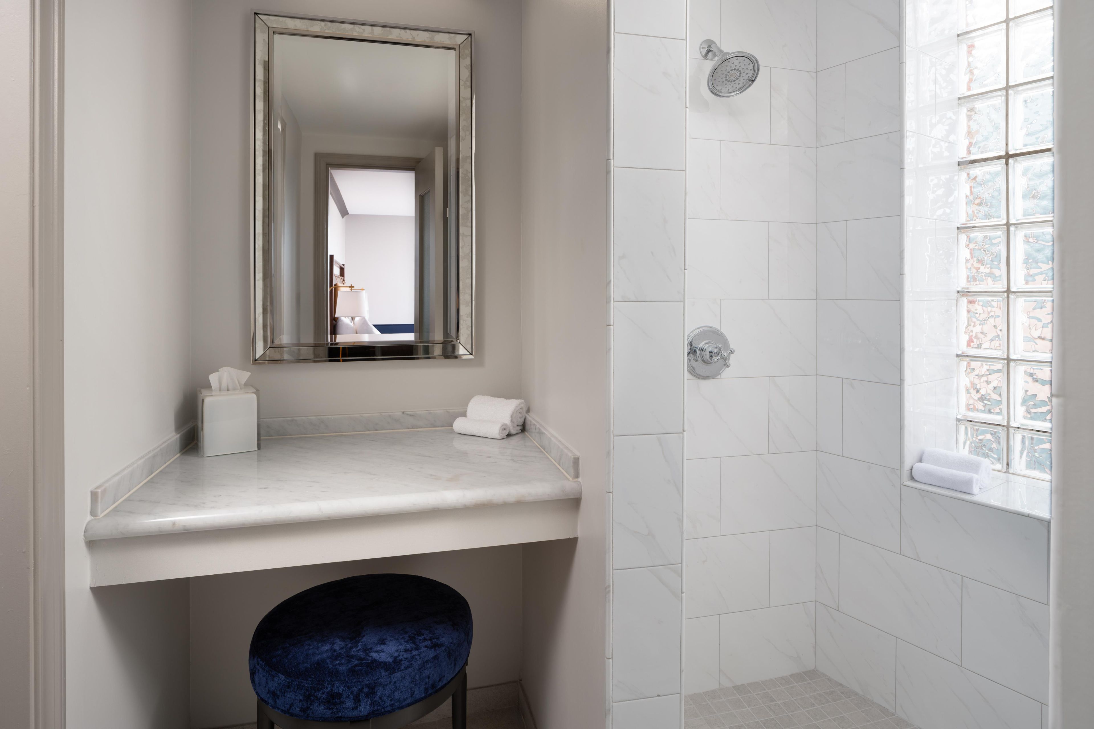 A bathroom with a marble countertop, a mirror, a towel rack, a shower with a glass door, and a window with a view.