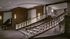 Un magnifique escalier avec des balustrades blanches, des marches recouvertes de moquette et un piano en arrière-plan.