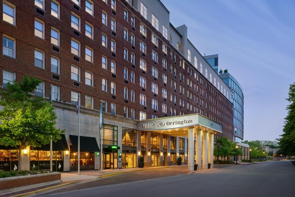 A hotel with a brick facade, a modern glass building to the right, and a well-lit entrance.