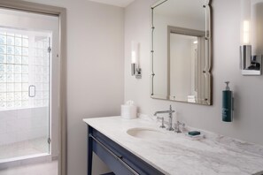 A bathroom with a marble sink, a large mirror, a towel dispenser, and a glass shower enclosure. - Hilton Orrington / Evanston (Evanston)