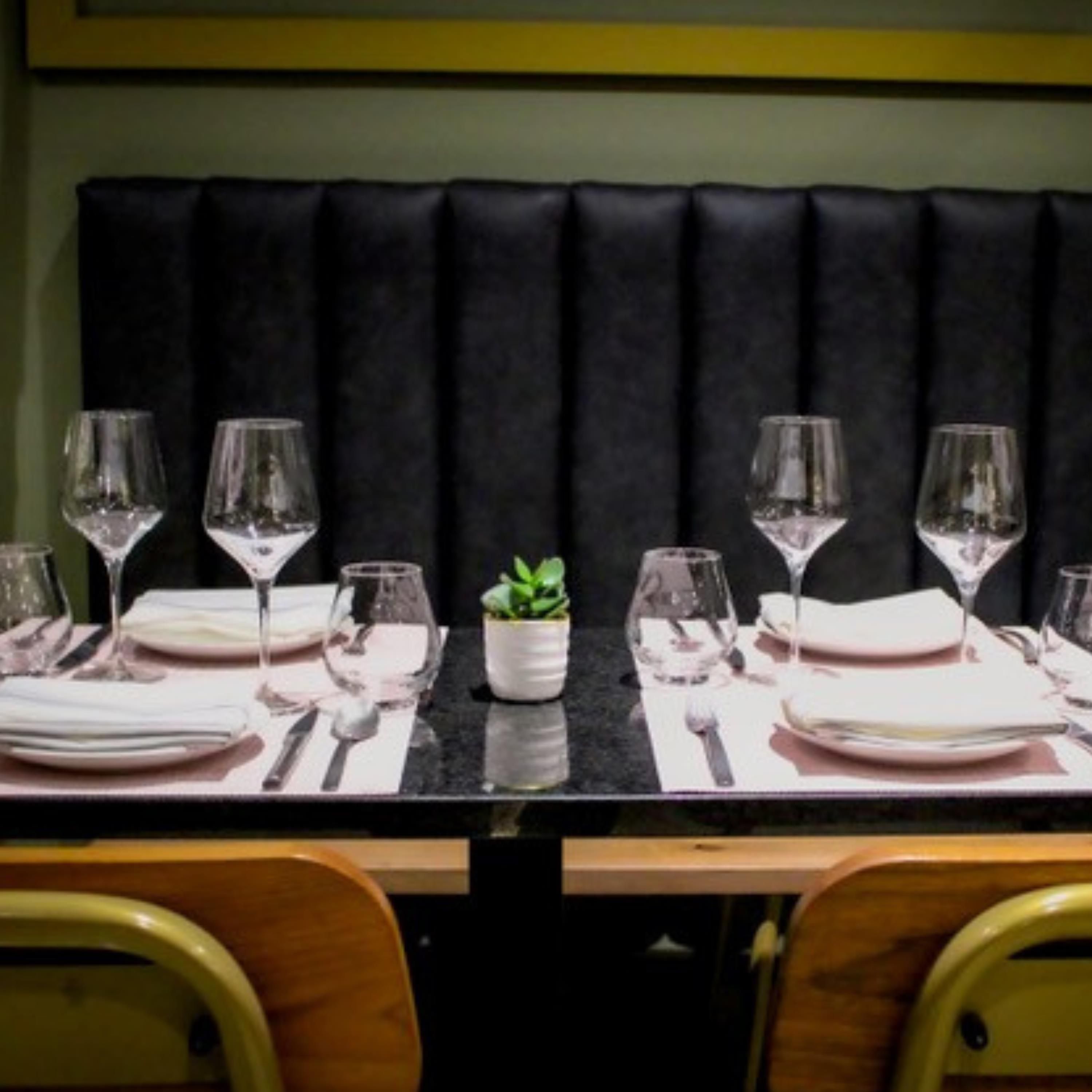 A dining table set with plates, cutlery, and wine glasses, flanked by wooden chairs.