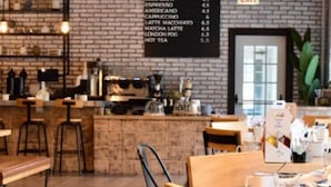 A café interior with a menu board, wooden tables, chairs, and a brick wall. - Hilton Orrington / Evanston (Evanston)