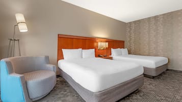 Habitació d'hotel amb dos llits, una cadira, una làmpada i una tauleta de nit.