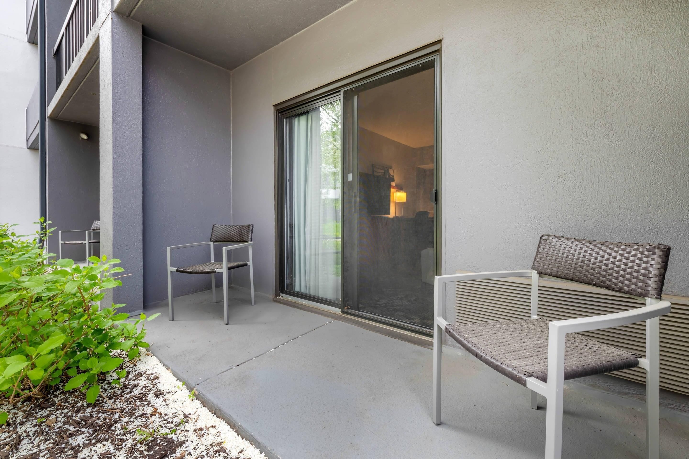 Een balkon met een stoel, een tafel, een schuifpui en een plant.