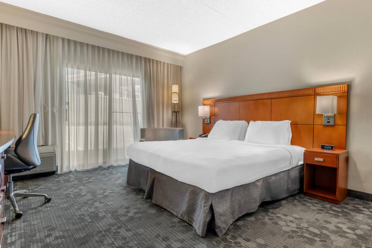 Una habitación de hotel con una cama grande, un escritorio con silla, una lámpara y una mesita de noche.