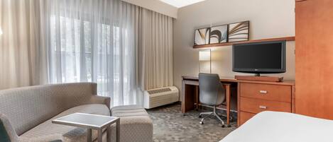 Habitación de hotel con sofá, una mesita, escritorio con silla, televisión y armario.