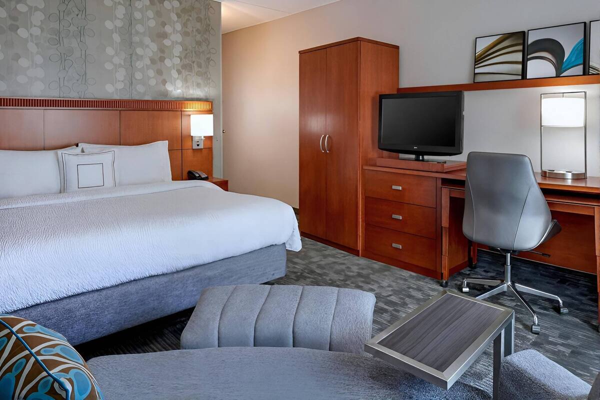 Una habitación de hotel con cama, escritorio, silla, televisor y armario.