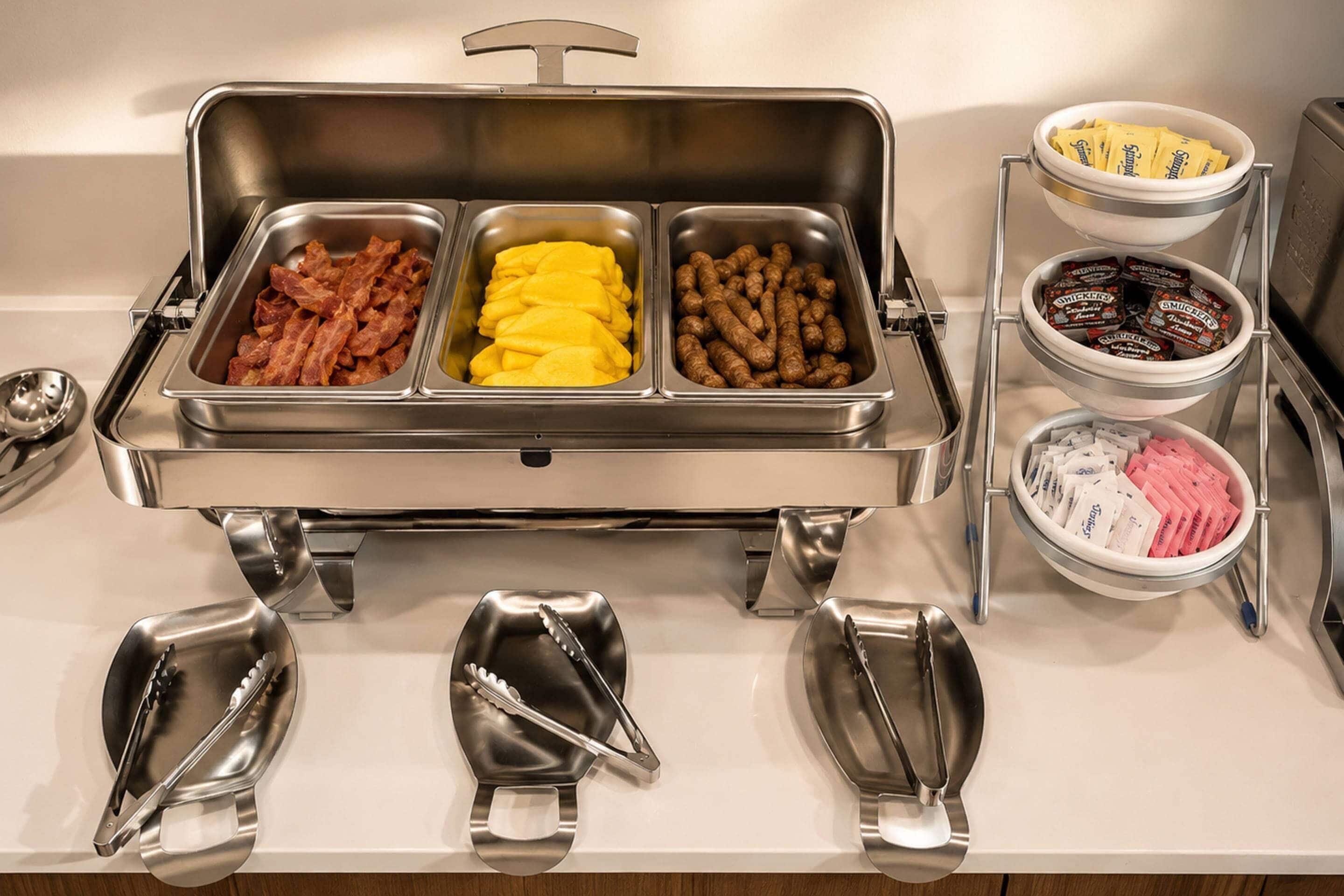 Un buffet proposant une variété de plats, notamment du bacon, du fromage jaune et des saucisses.