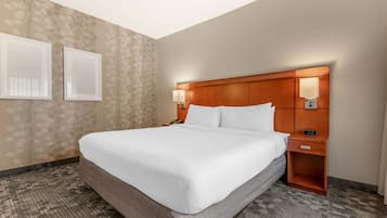 Una habitación de hotel con una cama grande, dos lámparas de noche, una mesita de noche con un reloj y un papel tapiz estampado.