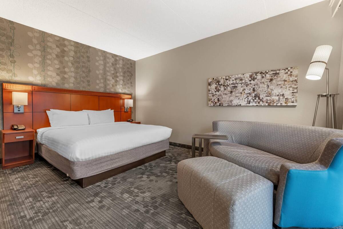 Una habitación de hotel con una cama, una mesita de noche, un escritorio, una silla y una lámpara de pie.