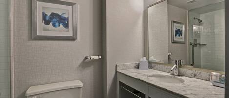 A modern bathroom with a white tiled wall, a marble sink, a toilet, and a framed artwork above the sink.