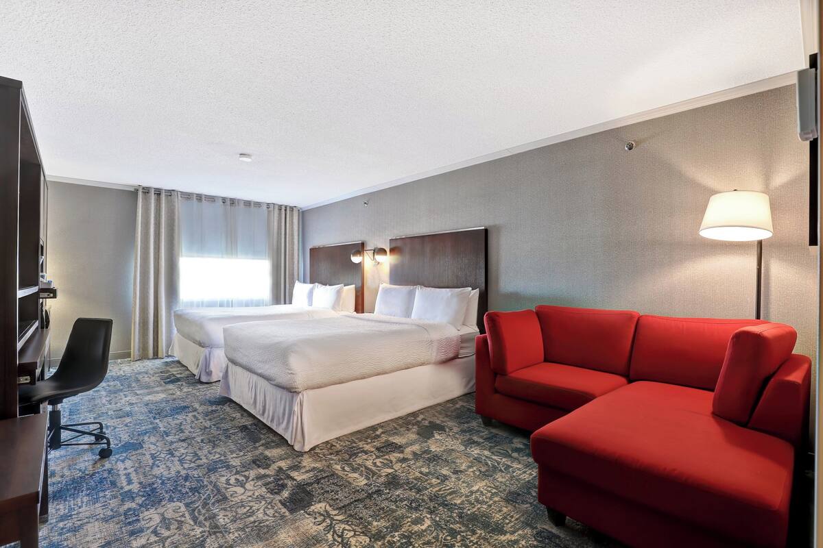 A hotel room with a large bed, a red sofa, a desk, and a lamp.