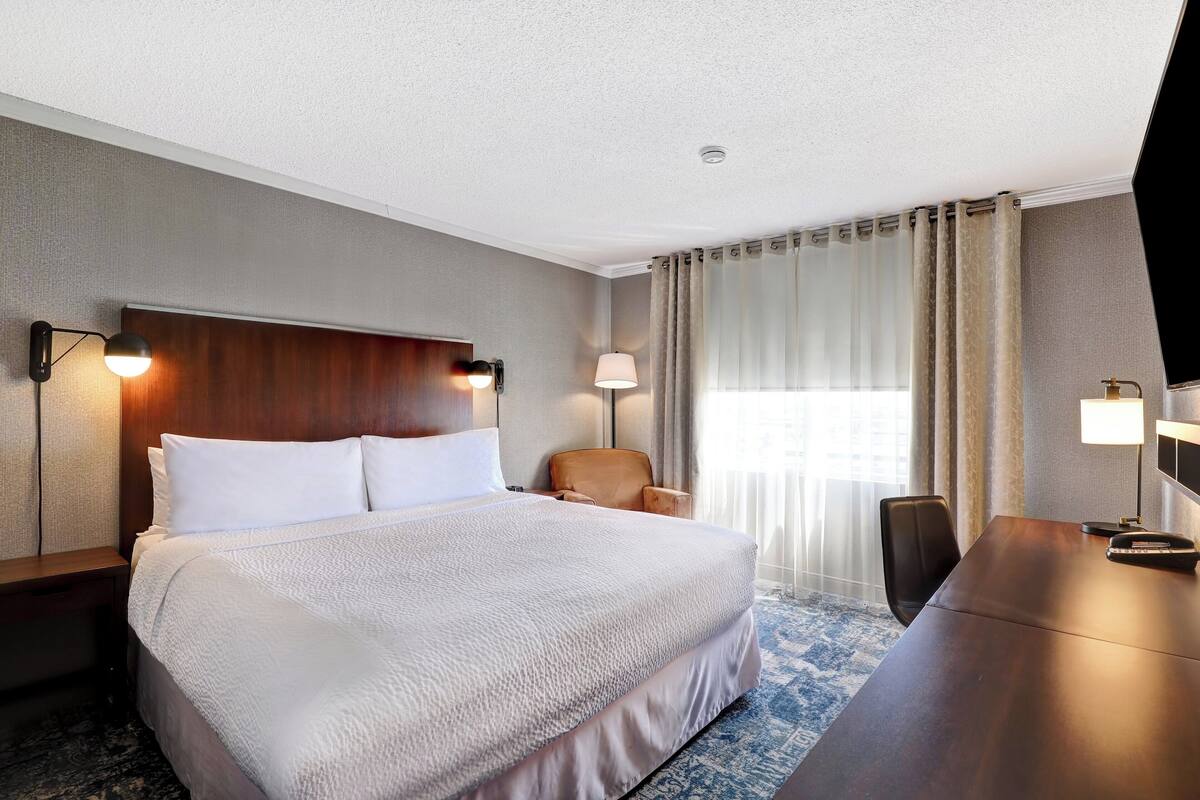 A hotel room with a large bed, a desk, a chair, and a TV.