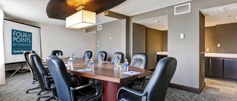 A conference room with a large table, black chairs, and a projector screen.