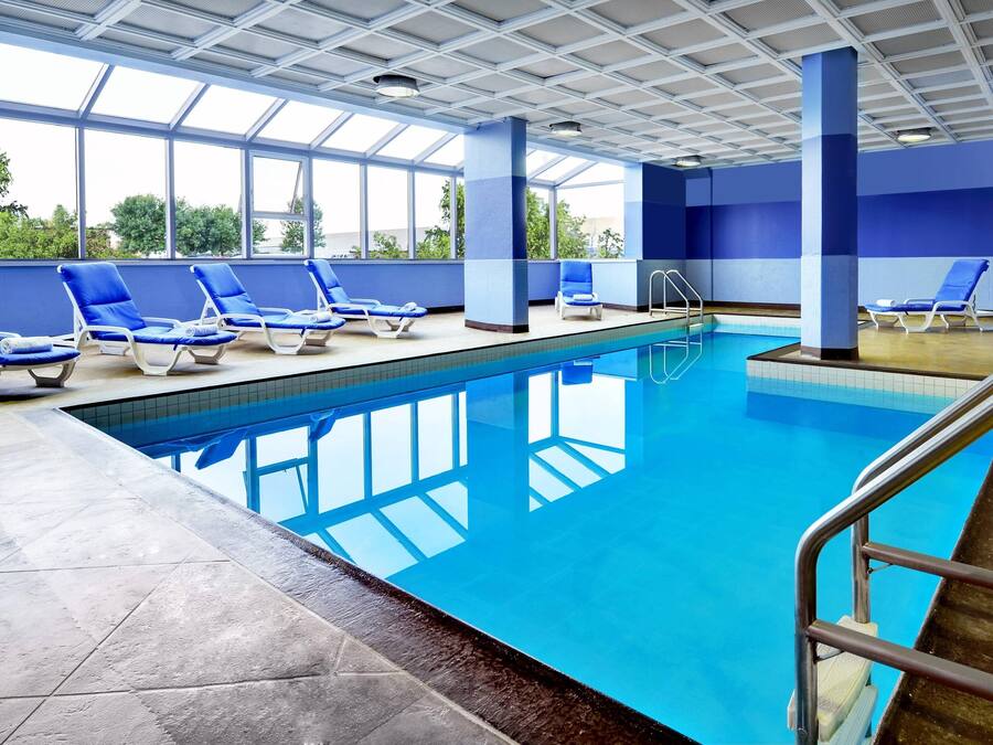 An indoor swimming pool with clear blue water, surrounded by blue lounge chairs and a tiled floor.