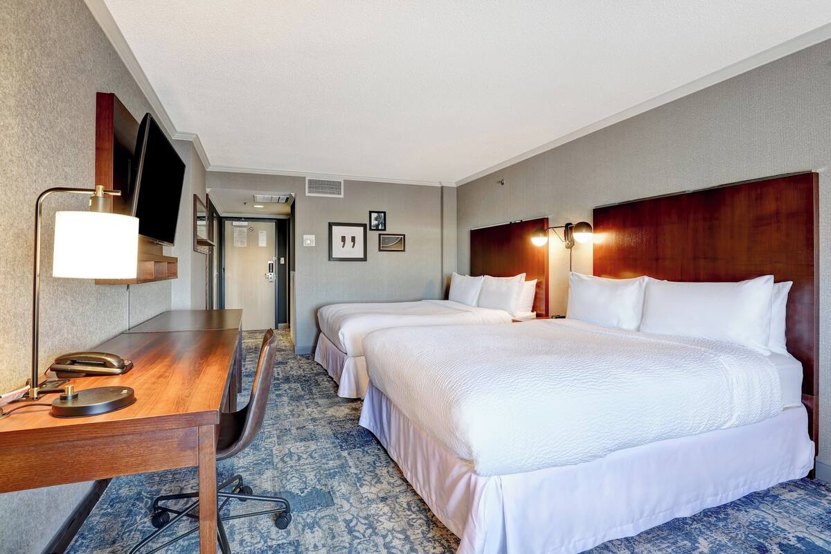 A hotel room with two beds, a desk with a telephone, and a television mounted on the wall.