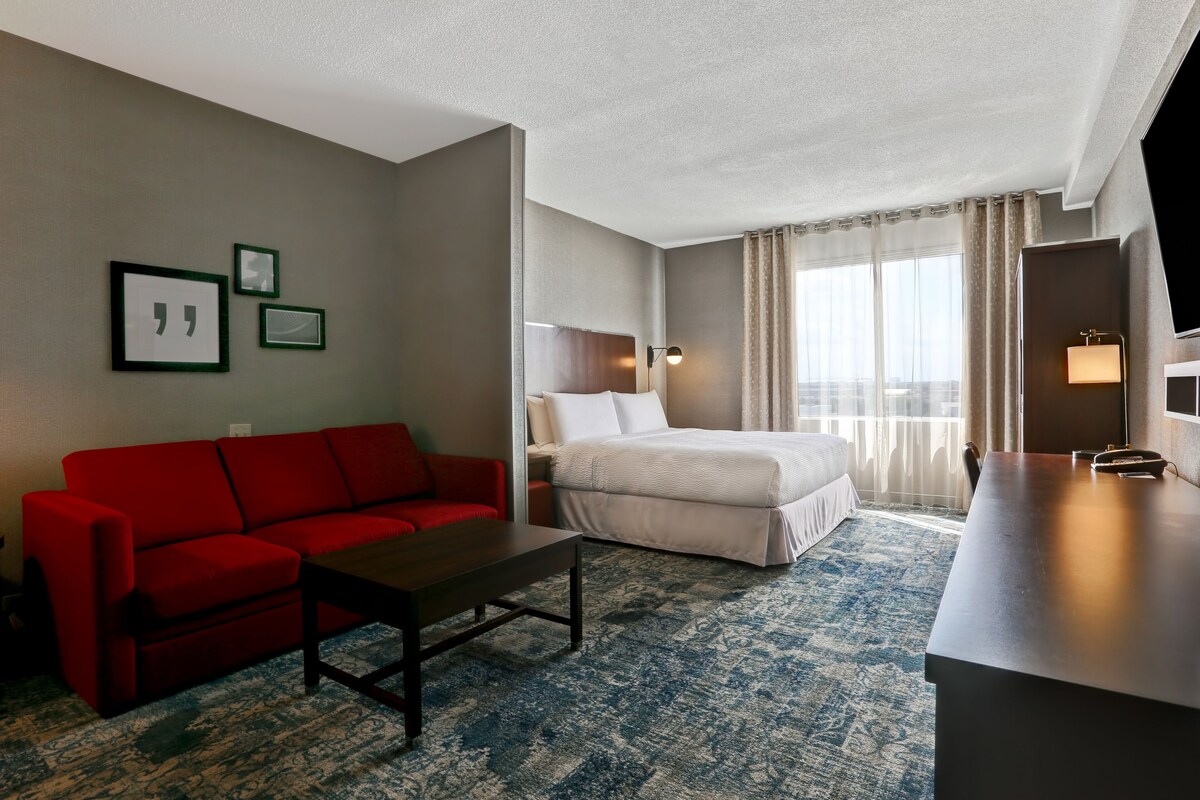 A hotel room with a red sofa, a bed, a desk, and a large window with curtains.