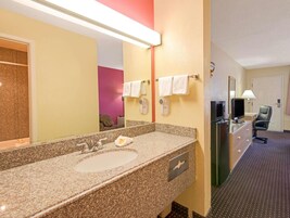 A hotel bathroom with a granite countertop sink, a mirror, a towel rack, a hairdryer, and a television.