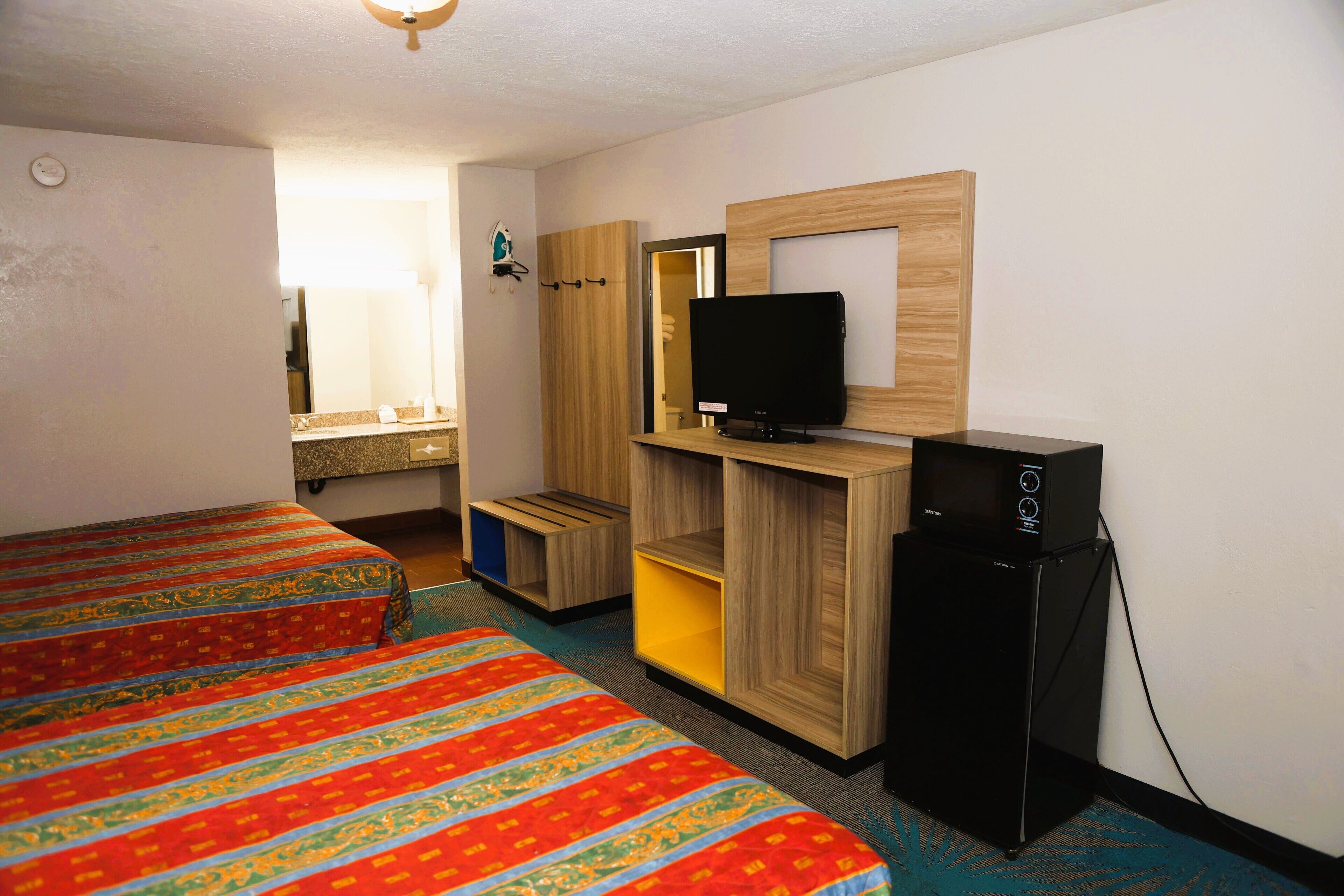 Une chambre d’hôtel avec deux lits, une télévision, un petit réfrigérateur et une armoire en bois.