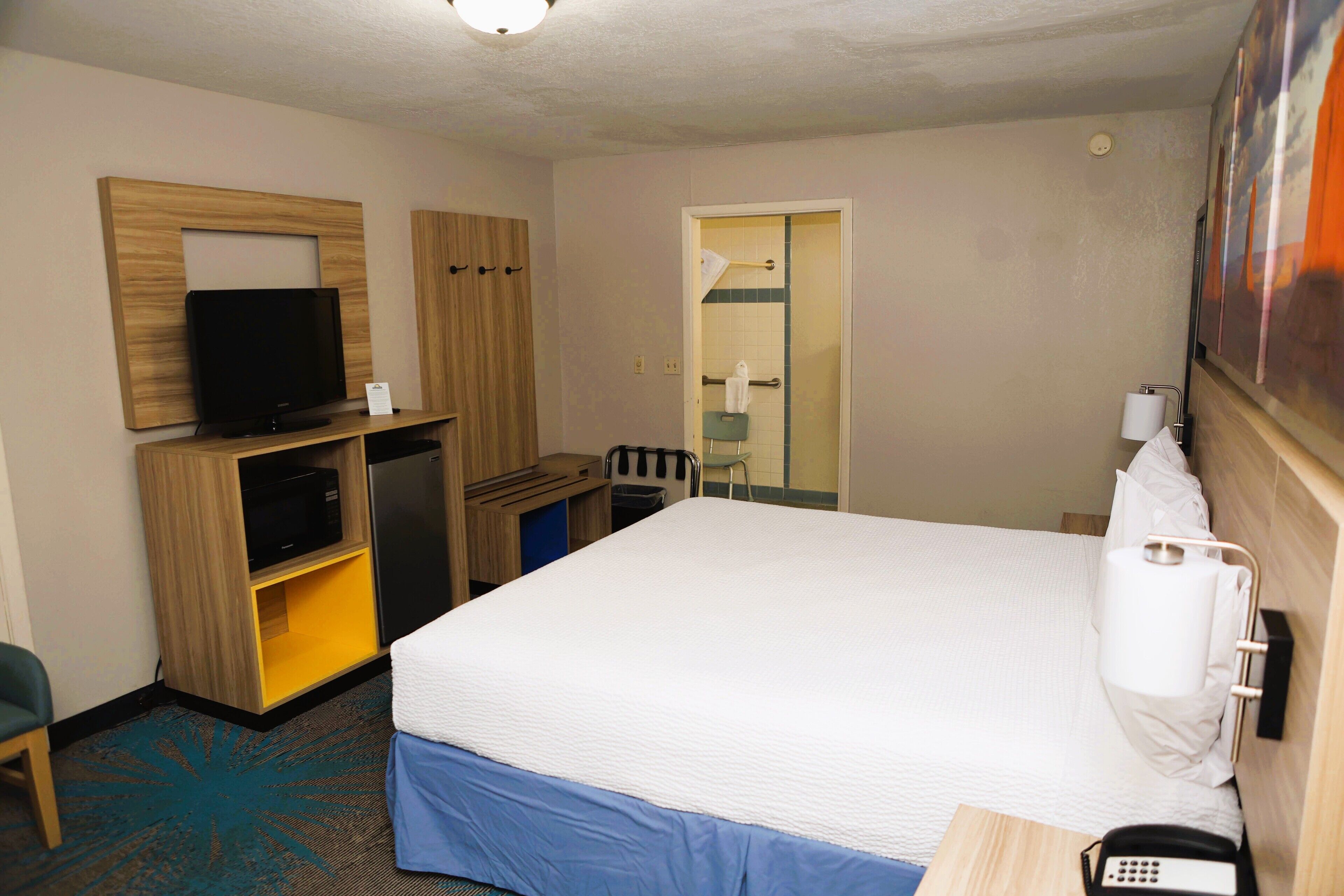 A hotel room with a bed, a desk with a telephone, a television, a mirror, and a door with a towel rack.