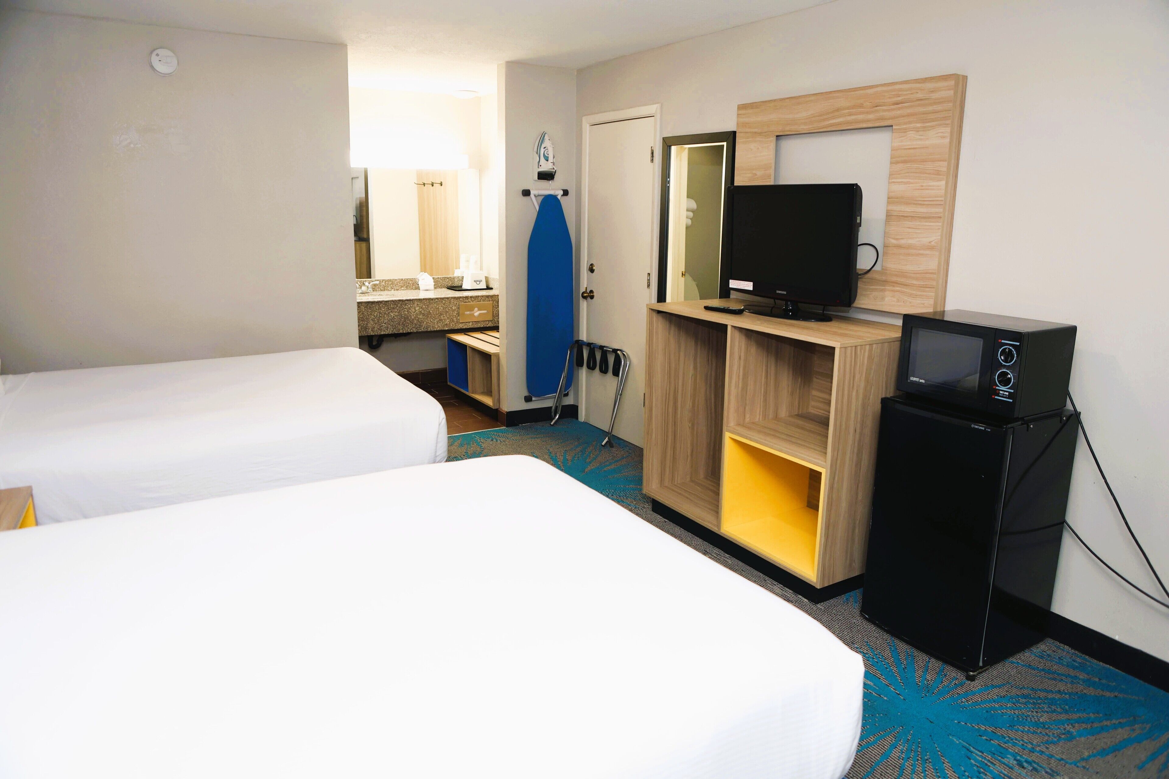 A hotel room with two beds, a television, a small refrigerator, and a bathroom visible through an open door.