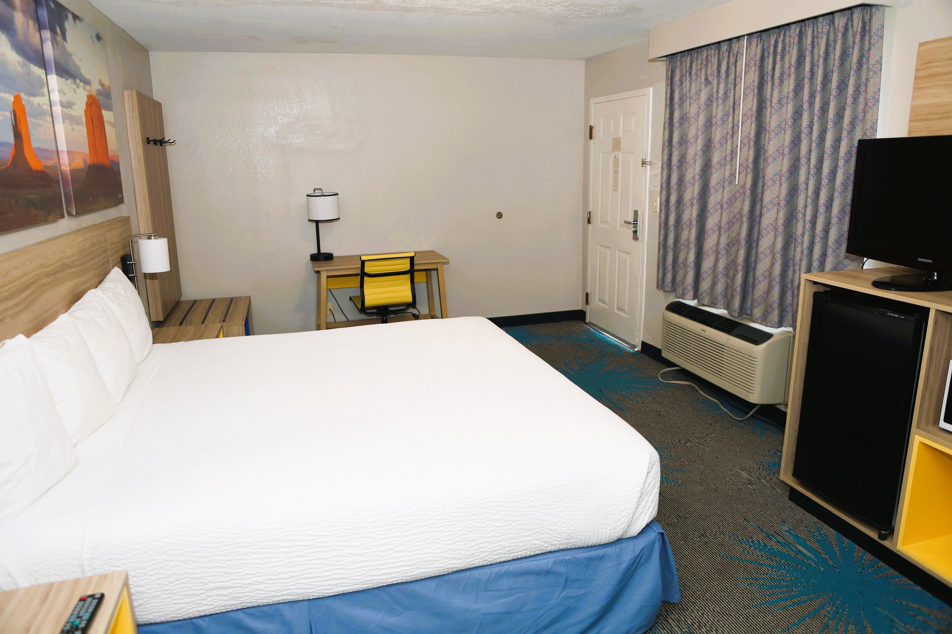 A hotel room with a large bed, a desk with a chair, a television, and a heater.