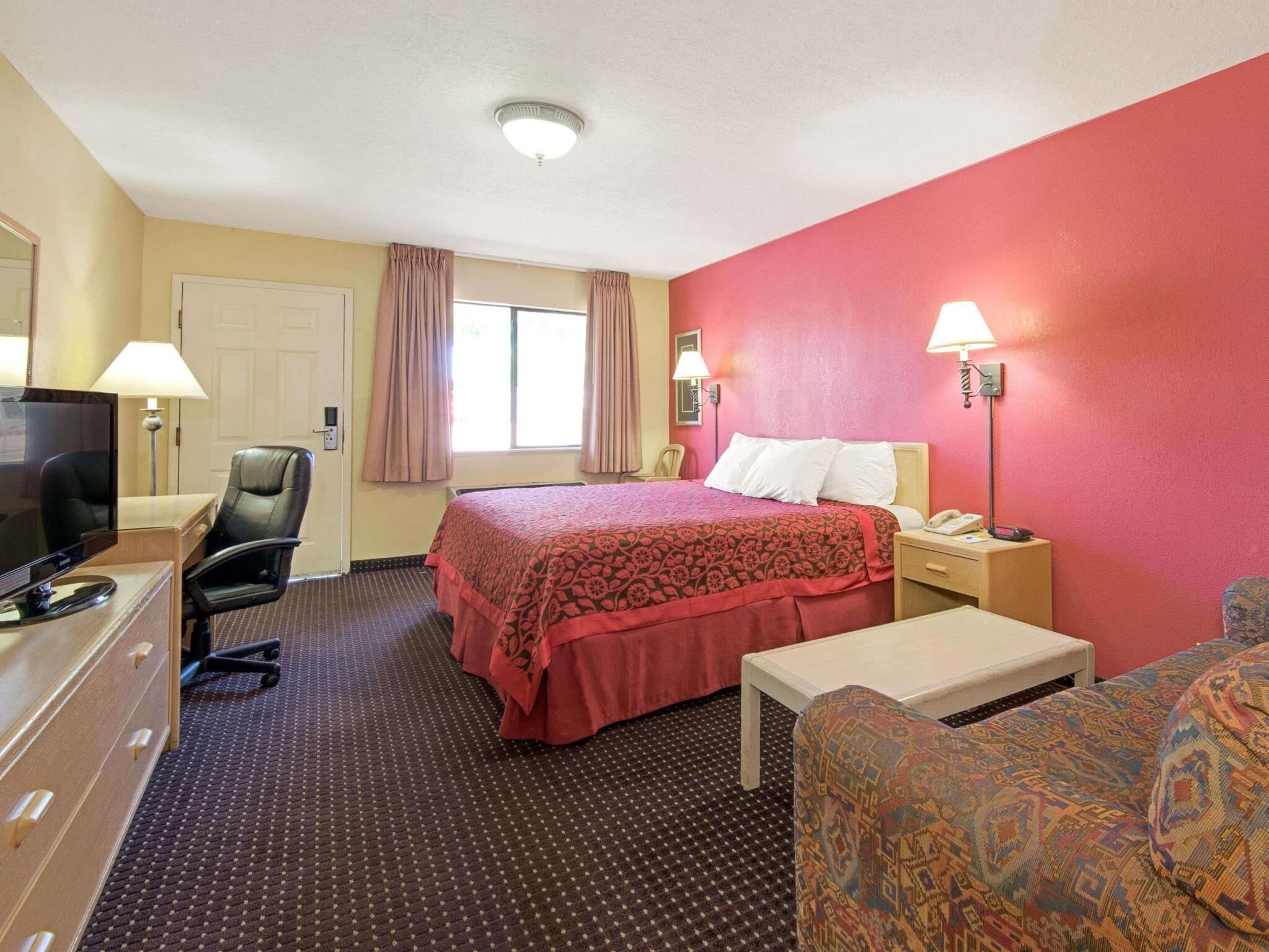 A hotel room with a bed, desk, chair, television, and lamps.