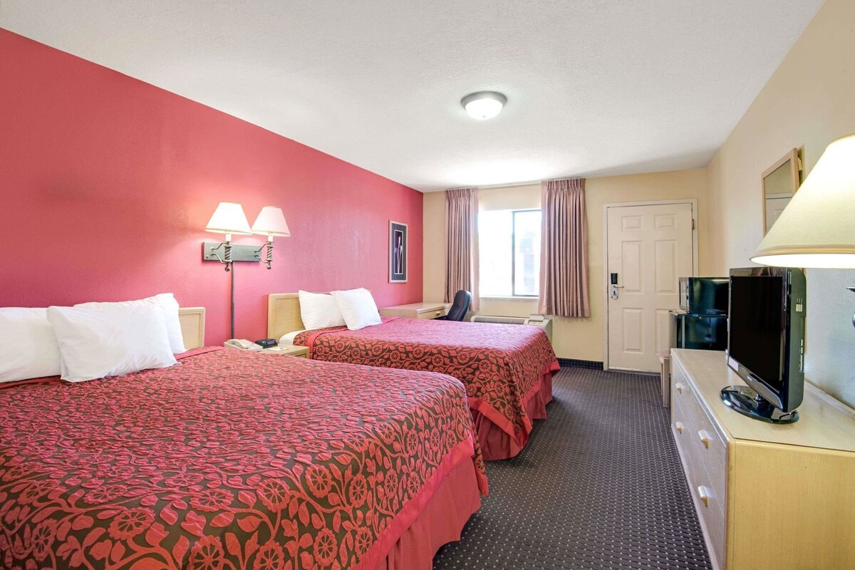 Une chambre d’hôtel avec deux lits, un bureau avec un ordinateur, une télévision et une fenêtre avec des rideaux.