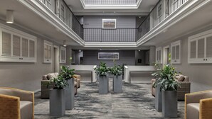 Un vestíbulo amplio con techo alto, un mostrador de recepción central y varias áreas de descanso con plantas en macetas.