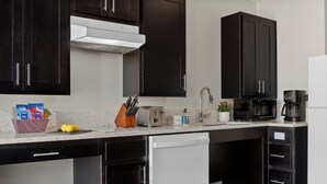Una cocina moderna con armarios oscuros, un lavavajillas blanco, un microondas y una cafetera.