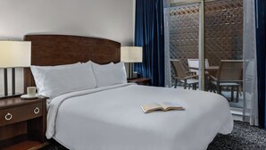Una habitación de hotel con una cama grande, dos lámparas de noche, una mesita de noche, una taza y un libro abierto.