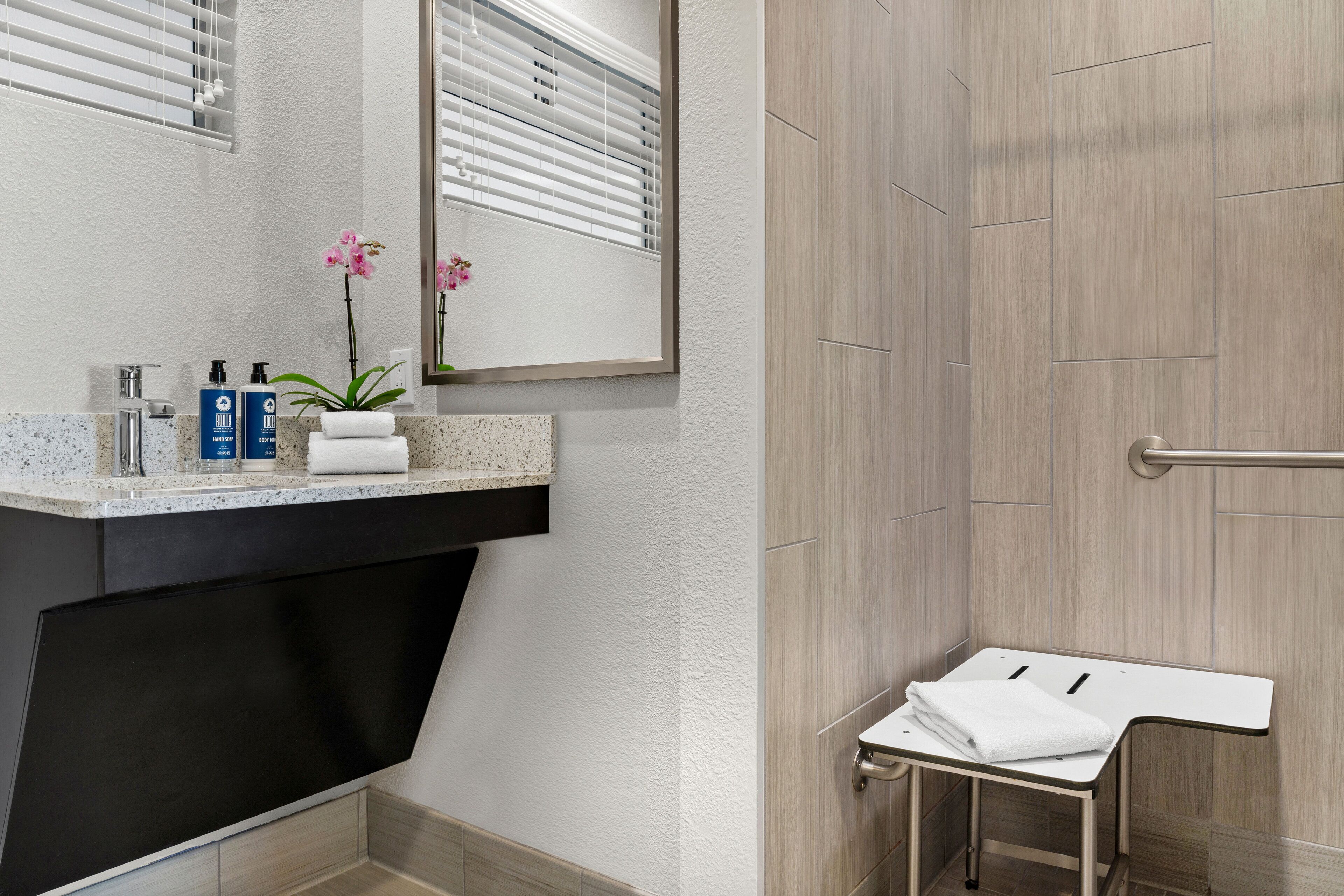 A modern bathroom with a granite countertop, a black sink, a mirror, and a shower area.