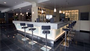 A modern bar area with a central counter, multiple bar stools, pendant lighting, and a visible wine rack in the background. - Nordsee Hotel Bremerhaven City (Bremerhaven)