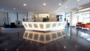 A modern reception area with a central counter, seating area, and large windows. - Nordsee Hotel Bremerhaven City (Bremerhaven)