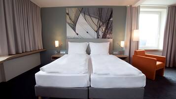 A double bed with white linens, a nightstand with a lamp, an orange chair, and a painting on the wall.