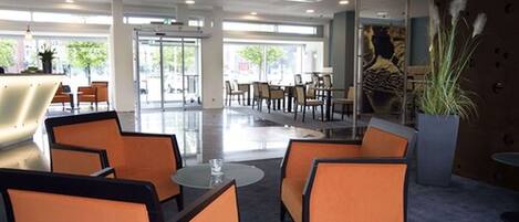 A modern lobby with orange seating, glass doors leading outside, and a large plant.
