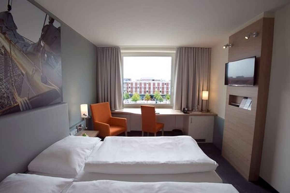 Habitación de hotel con cama, dos sillas, escritorio, televisión y ventana con vista a edificios.