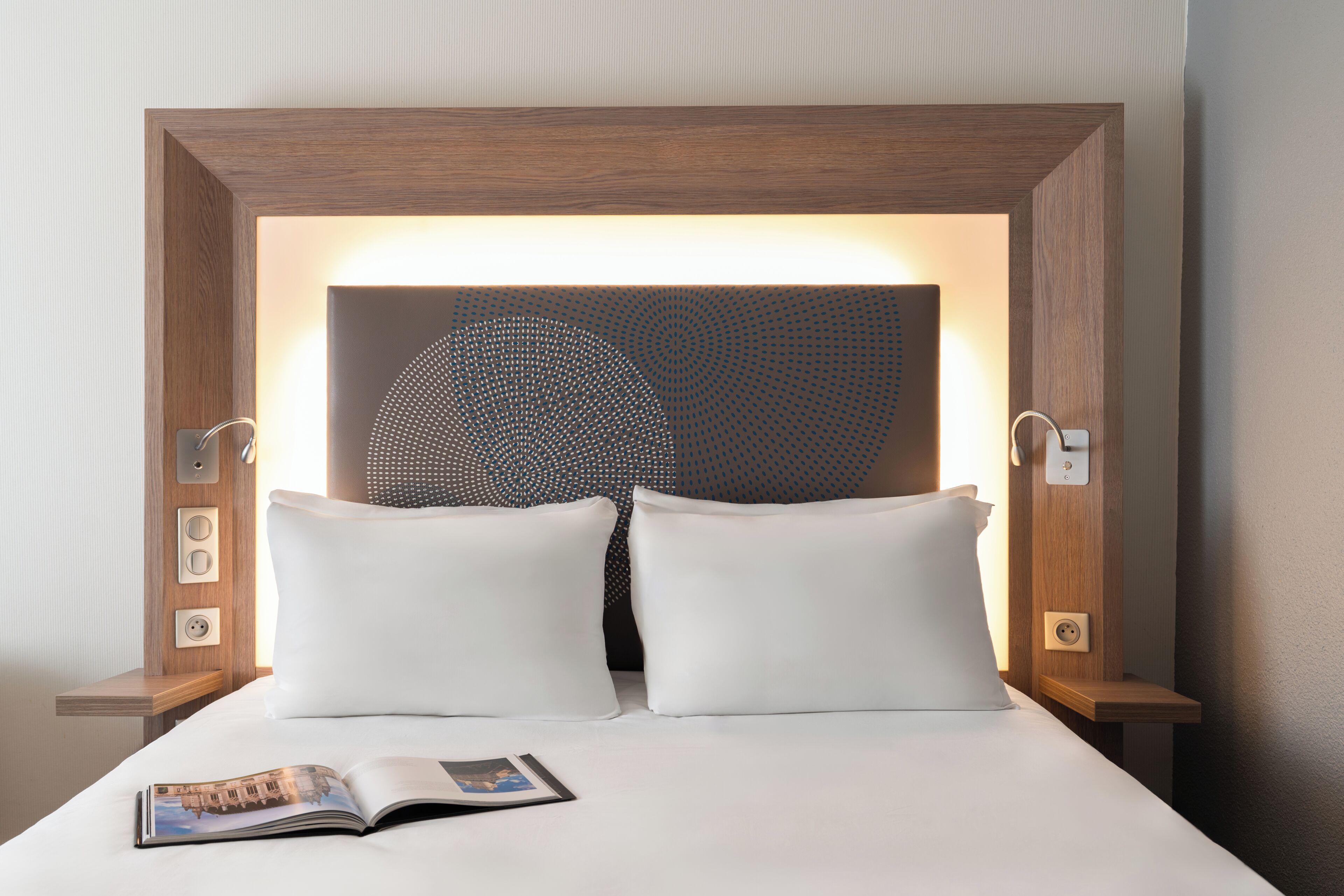 Una cama bien hecha con sábanas blancas, una sola almohada y una revista encima.
