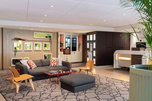A modern living room with a sofa, coffee table, and chairs, a kitchen area with cabinets, and a large potted plant.