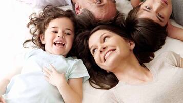 A family of four lying on a bed in a room.