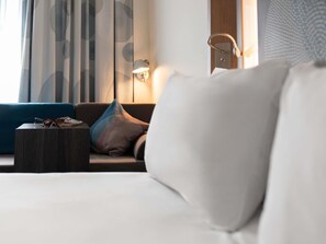 Ein Hotelzimmer mit Bett, Nachttisch, Lampe und einem Fenster mit Vorhängen.