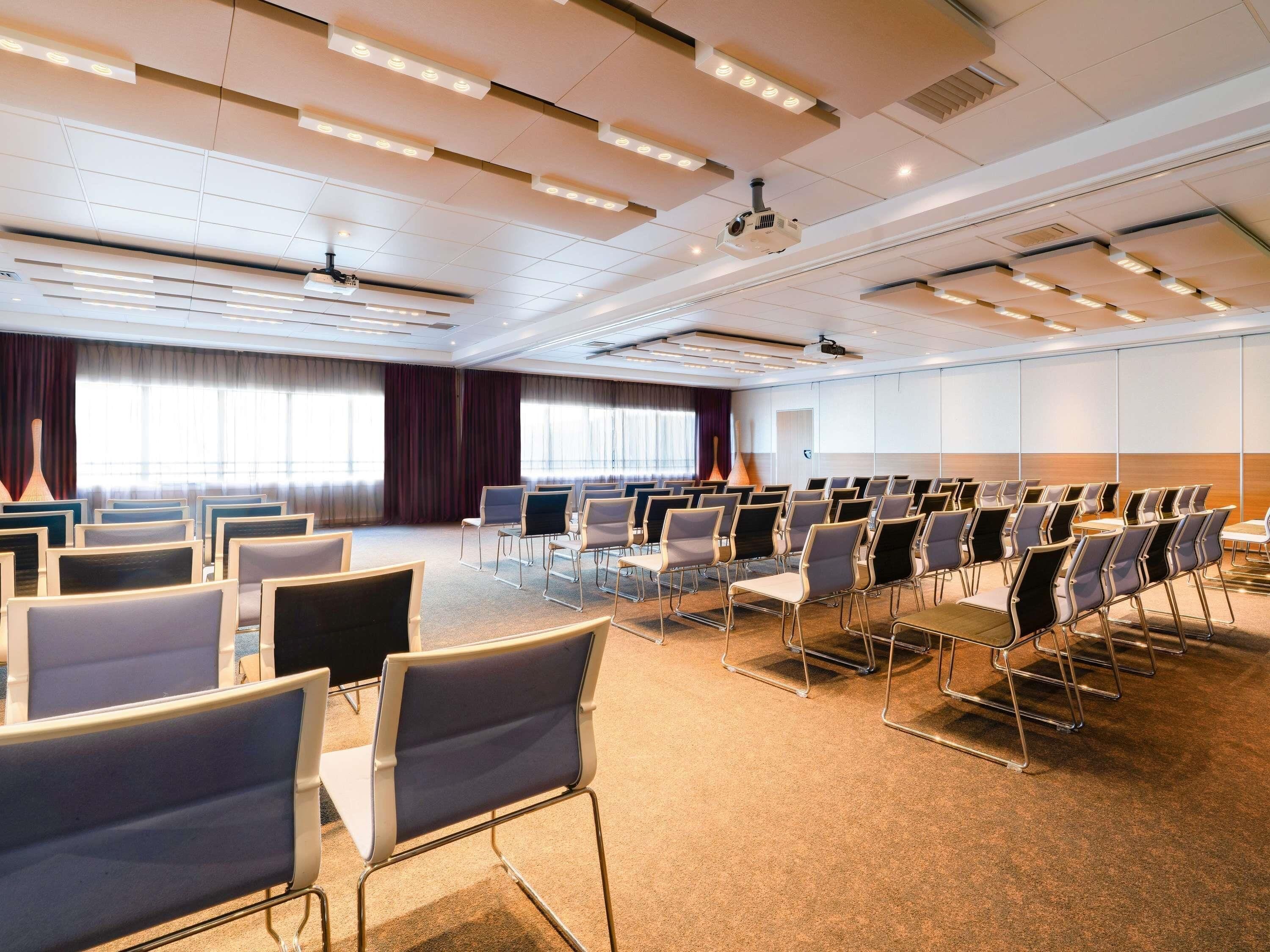 A conference room with rows of chairs, a projector, and a large screen.