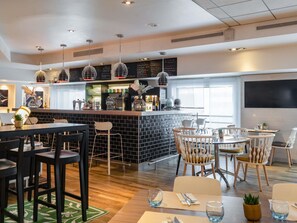 A modern bar area with a black-tiled counter, hanging pendant lights, and a barista preparing drinks.