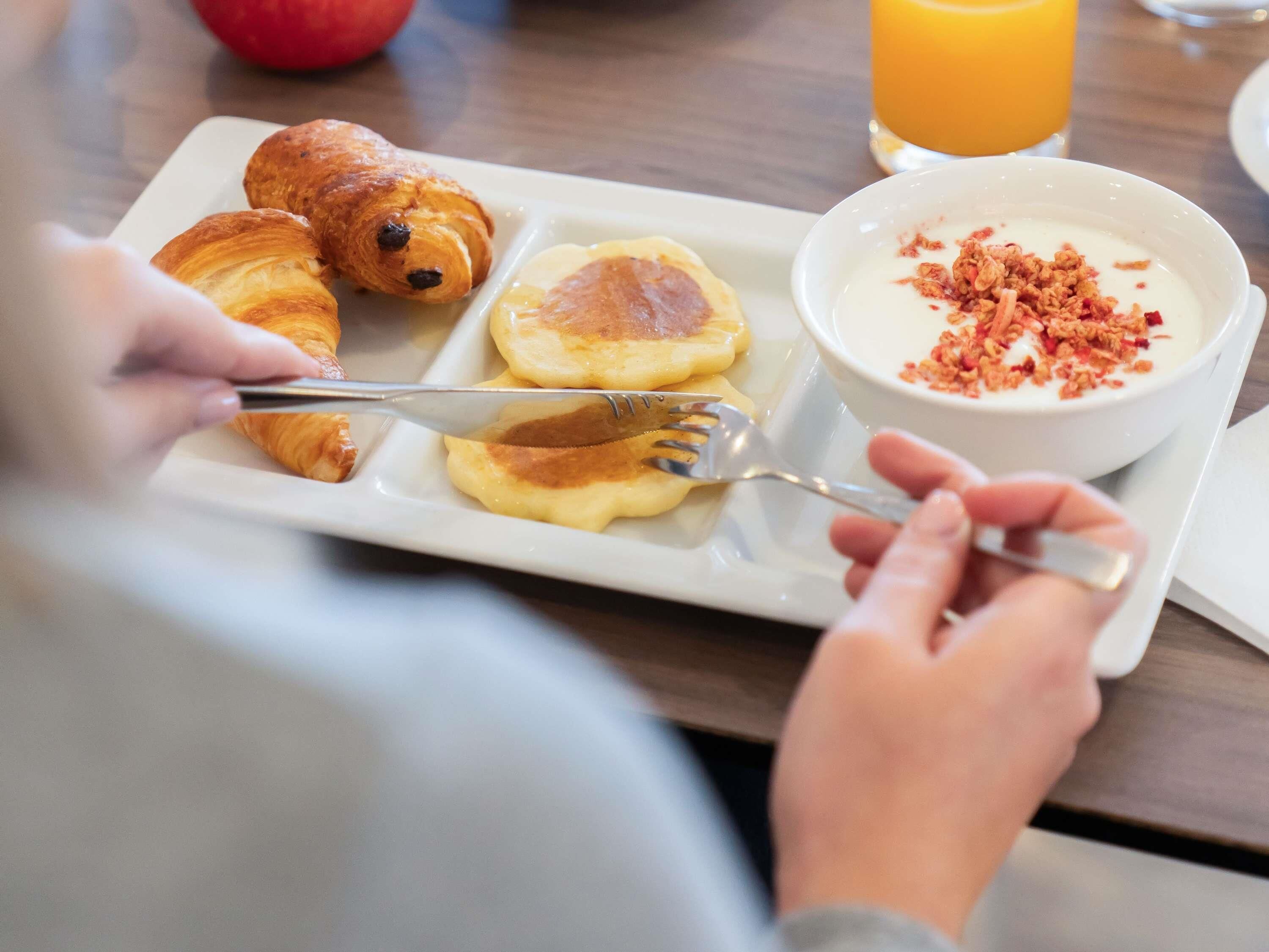A breakfast tray with croissants, pancakes, and a bowl of yogurt with granola.