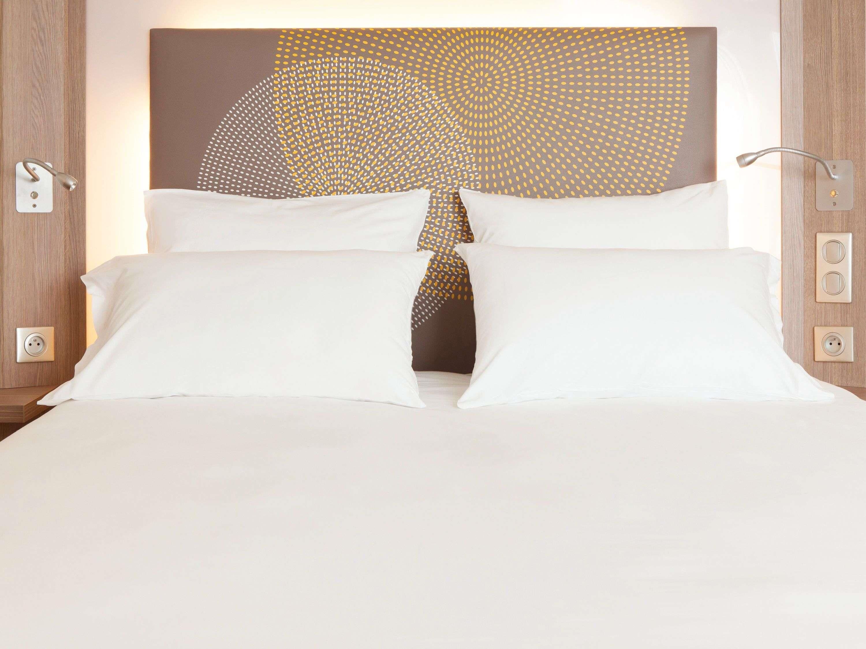 A neatly made bed with white linens, a modern abstract wall art piece above it, and a wooden headboard.