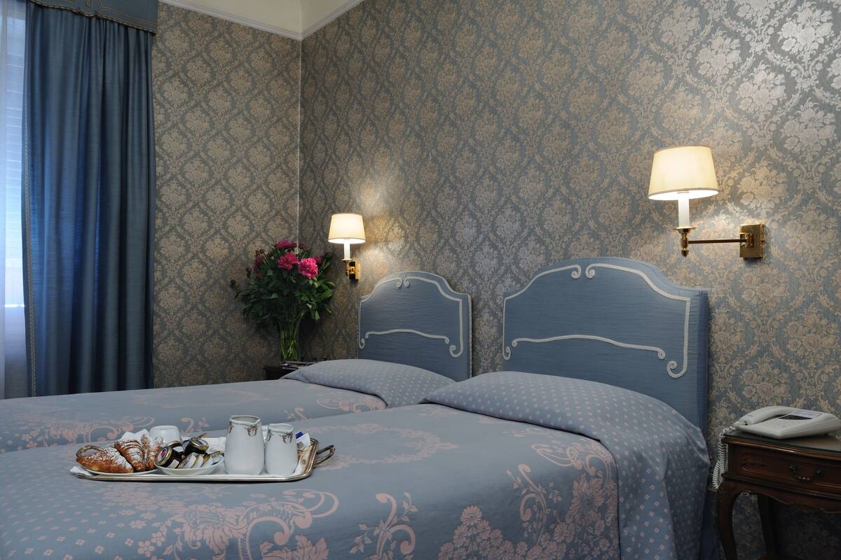 A hotel room with a bed, two wall-mounted lamps, a tray with breakfast items, and a phone on a bedside table.