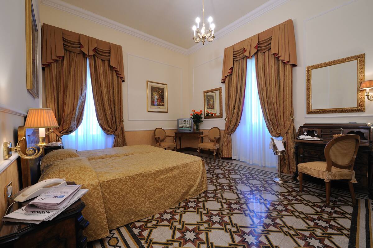 A hotel room with a large bed, a desk with a telephone, a chair, a desk lamp, and a mirror.