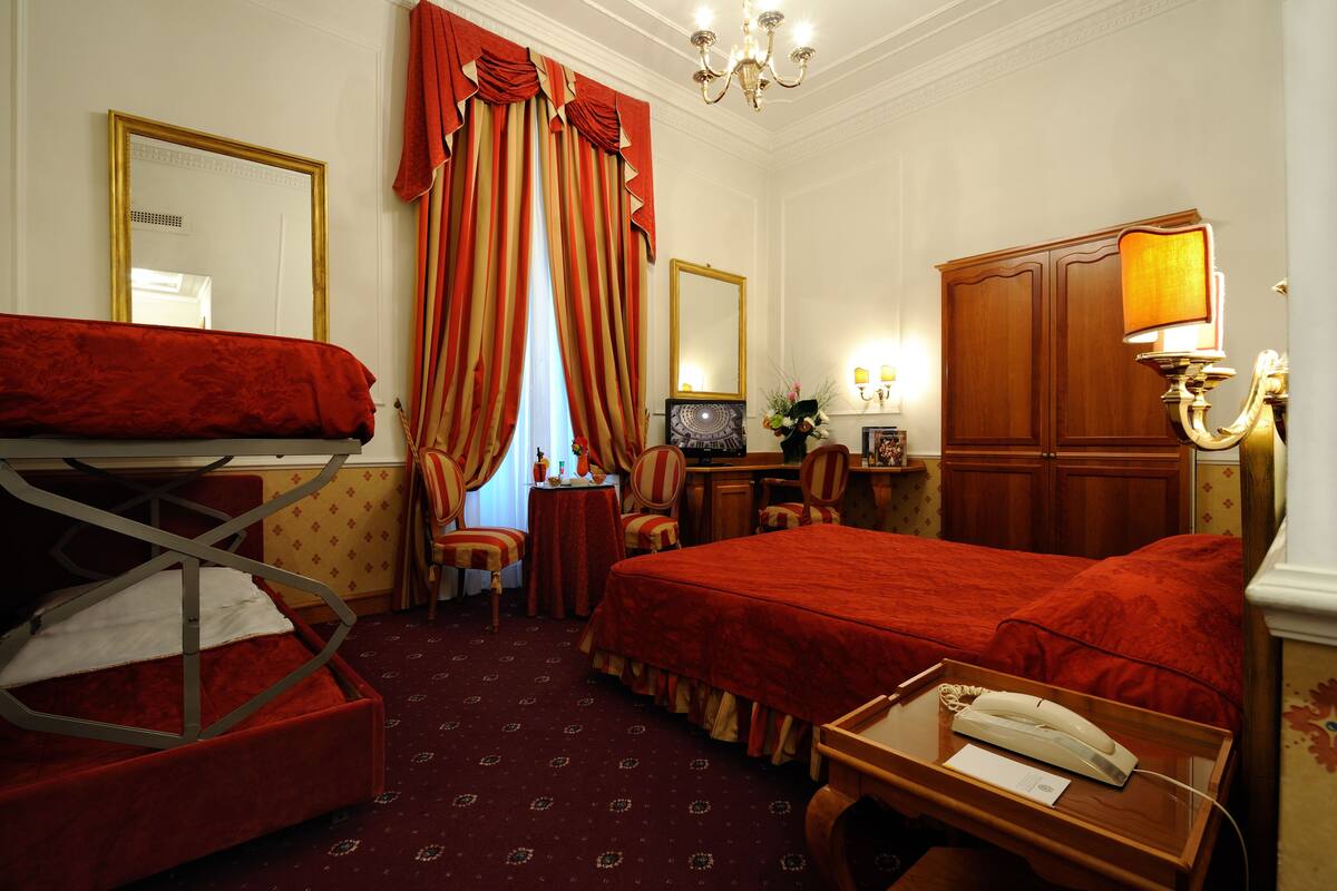 A hotel room with a bed, a desk with a telephone, a chair, a small table, and a television.